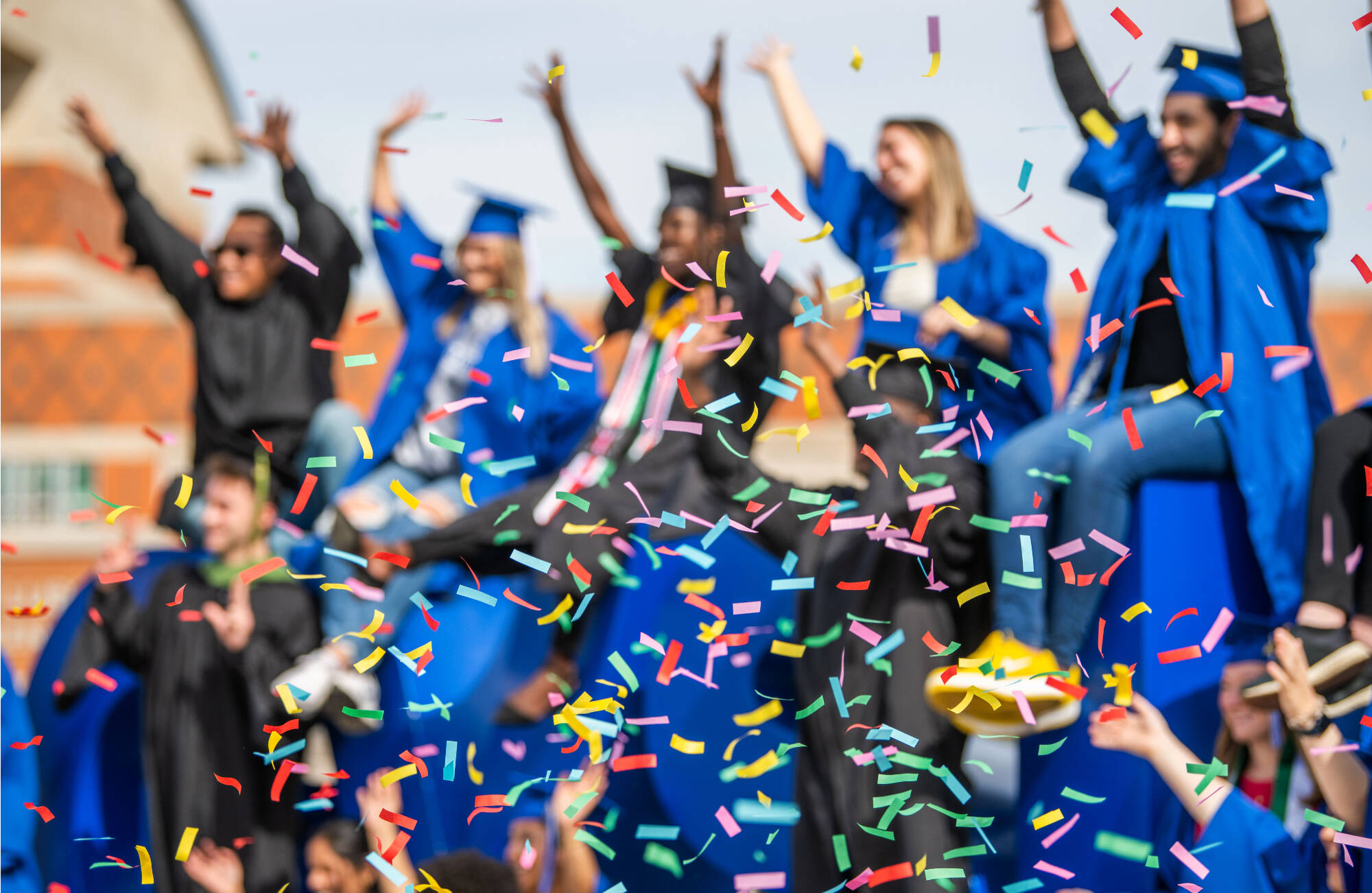 Students celebrating graduation in caps and gowns with confetti.